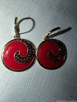 Front view of both earrings showing red enamel surfaces and rhinestone swirl