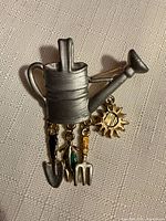 Front view of silver-tone watering can brooch with dangling charms