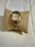 Front view of gold-tone cuff quartz watch on display pillow