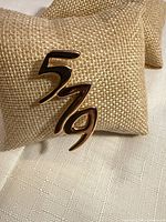 Front view of goldtone brooch displaying 5-7-9 design