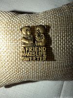 Front view of goldtone pin showing design and text