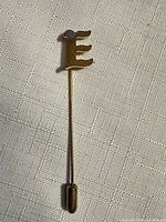 Full view of gold-tone stick pin with letter “E” top and clutch cap
