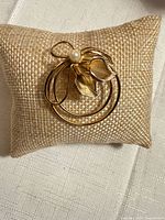 Front view of gold-tone double-circle brooch with pearl and leaf design on burlap cushion