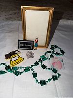 All items laid out: gold frame, welcome badge, woman pin, yellow bottle opener, amethyst figurine, green bead necklace, ceramic tile