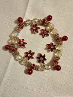 Bracelet laid flat showing clear beads, red poinsettia charms, spacer and round beads