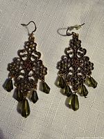 Pair of goldtone filigree chandelier earrings with green teardrop crystals displayed on fabric