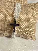 Bracelet front view on display pillow showing silver-tone cross and white cord
