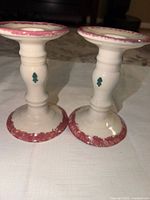 Front view of both matching ceramic candlestick holders showing cream glaze, pink trim, and green tree motif