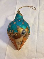 Front view showing teal quilted top, gold trim, rhinestone and cream-gold bottom