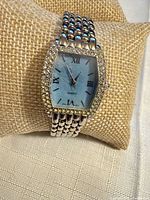 Front view of silvertone wristwatch on cushion showing blue dial and rhinestone bezel