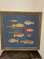 Front view of framed needlepoint showing nine fish on blue background
