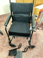 Overall view of folded transport wheelchair with cushion and detached footrests