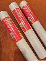 Three sealed B&Q Value Woodchip wallpaper rolls on orange surface