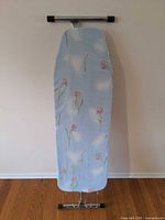 Ironing board folded upright showing cover pattern and frame ends