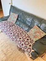 Front view of green leather sofa with cushions and crochet throw