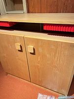 Front view of closed cabinet showing veneer finish, block handles and red drawer fronts in upper compartment