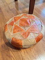 Full view of orange/tan leather pouf on wood floor