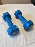 Pair of blue vinyl 5 lb hex dumbbells on cloth surface