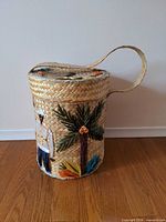 Front view of cylindrical raffia basket showing tropical appliqué and lid with strap