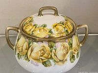 Covered porcelain bowl with lid on, showing floral design and gold handles