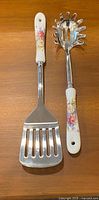 Front view of both utensils showing stainless heads and floral ceramic handles