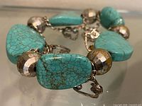 Bracelet laid flat showing turquoise slabs, faceted beads, chain and charms