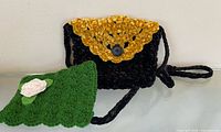 Black crochet sling bag with yellow flap and green crochet eyeglass case