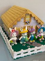 Front angled view of needlepoint house and four bunny figurines