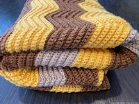 Folded crochet afghan showing layered yellow, brown and grey zig-zag stitches