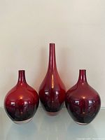 Front view of three ruby red glass vases