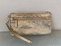 Front view of metallic gold leather wristlet clutch showing detachable strap and front zip pocket