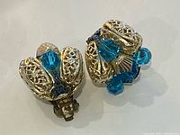 Front view showing gold-tone filigree petals and blue bead cluster detail