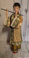 Full front view of 13-inch Asian woman doll in embroidered robe holding flute