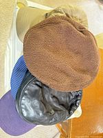 Stack of varied caps showing brown beret, black faux leather beret, purple and blue caps, tan cap