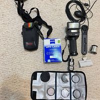 Top-down view showing entire lot: pouch, lens cloths, flash on grip with cable, quick-release plate, auxiliary lens, adapter, filter wallet