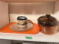 Group shot showing stacked decorative plates on orange tray beside amber Visions casserole with lid