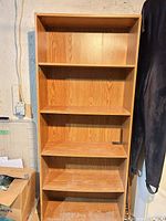 Full front view of tall oak-finish bookcase showing five shelves