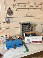 Overall lot on workbench: blue metal toolbox, hammer, parts drawer organizer, box of misc hardware