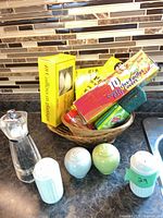 Overview of lot showing shakers, grinder, basket with boxed spoons, food covers and scouring pads