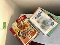 Two stacks of assorted cookbooks showing Campbell’s Dinner’s On! and community spiral cookbook on top