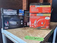 MotoMaster Eliminator charger box beside Motor Trend air compressor box on shelf