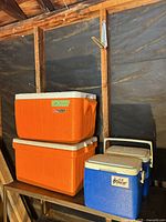 Stacked orange full-size Coleman Poly-Lite coolers and two blue Coleman Lil' Oscar personal coolers