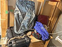Stack of luggage showing black roller, grey garment bag, blue backpack, tan duffel and other items