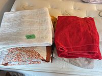 Stacked linens showing white blanket, quilt, red towels, grey/beige towel