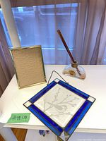 All three items: stained glass panel, reed diffuser with reeds, gold-tone frame on tabletop