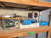 Shelf view showing boxed Logitech mouse, TomTom GPS, Dynex keyboard box and basket of loose cables