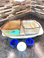 Group shot showing brown stoneware loaf pan, clear Pyrex loaf pan on top of white floral CorningWare casserole with three ramekins at front