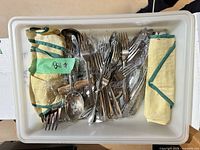 Bin containing mixed flatware, serving utensils, tongs, cloth rolls