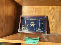 Front view showing frame, blue backing, brass ship’s wheel and anchors