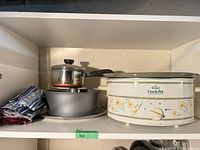 Shelf view showing slow cooker, saucepan on pan, blue striped linens